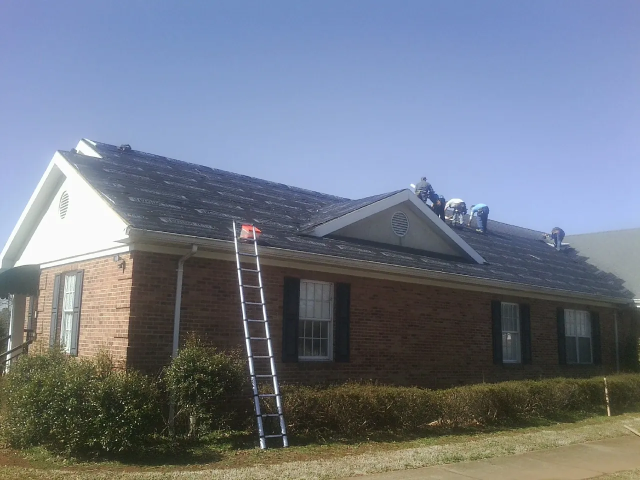 Crew tearing shingles off a brick ranch roof with a ladder set — Metal Roof Repair work by our crew in Luray